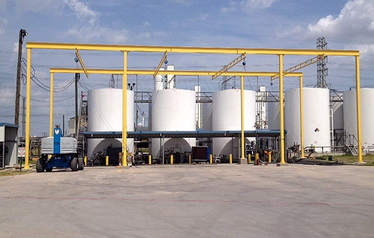 Yellow overhead rigid lifeline fall protection system at a bulk storage tank facility